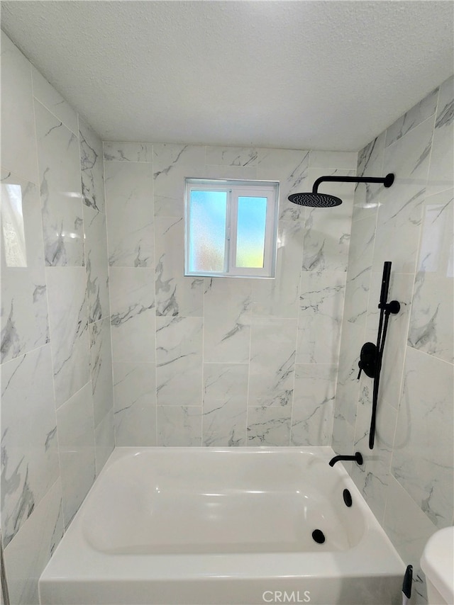 bathroom with a textured ceiling, toilet, and tiled shower / bath