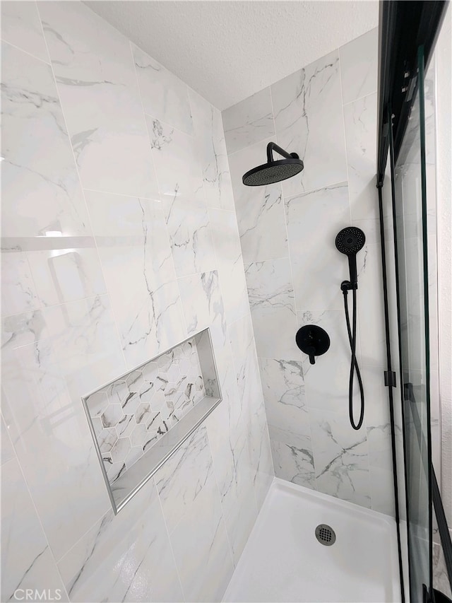 bathroom with a tile shower and a textured ceiling