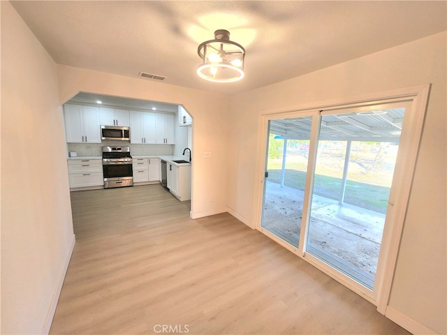 kitchen with sink, light wood-type flooring, white cabinets, and appliances with stainless steel finishes