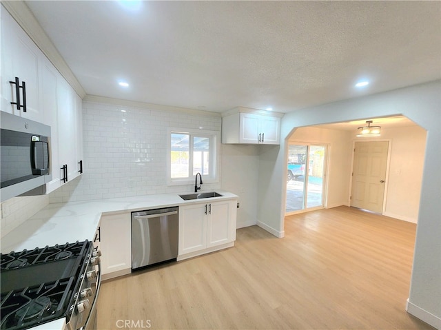 kitchen featuring white cabinetry, sink, light hardwood / wood-style floors, stainless steel appliances, and light stone countertops