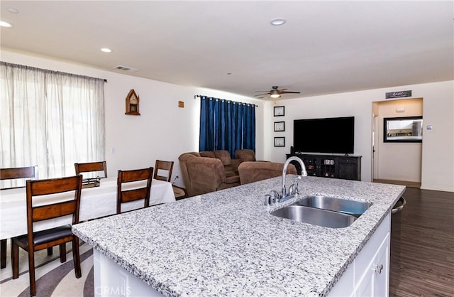 kitchen featuring sink, dark hardwood / wood-style floors, an island with sink, ceiling fan, and light stone countertops