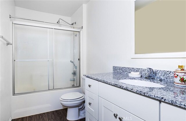 full bathroom featuring vanity, hardwood / wood-style flooring, enclosed tub / shower combo, and toilet