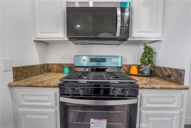 kitchen with dark stone counters, gas stove, and white cabinets