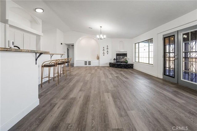 unfurnished living room featuring lofted ceiling, dark wood-type flooring, a chandelier, and french doors