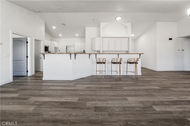 kitchen featuring lofted ceiling, a breakfast bar area, white cabinets, dark hardwood / wood-style flooring, and kitchen peninsula