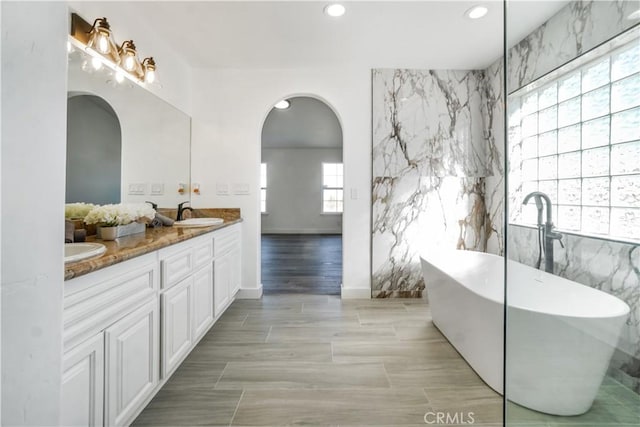 bathroom with a bathing tub, tile walls, and vanity