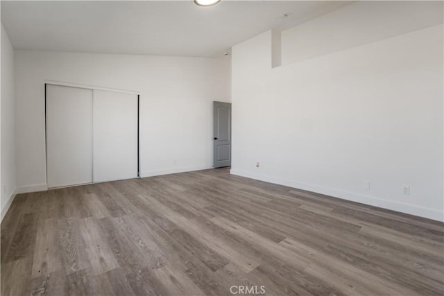 unfurnished bedroom with hardwood / wood-style floors, high vaulted ceiling, and a closet