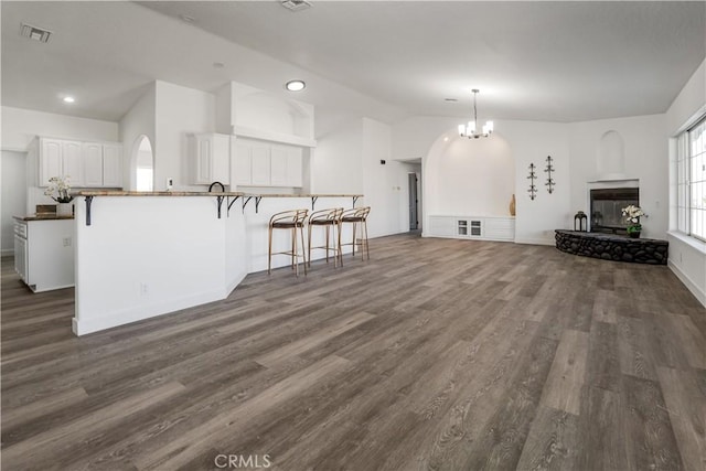 living room with a multi sided fireplace, lofted ceiling, an inviting chandelier, and dark hardwood / wood-style flooring