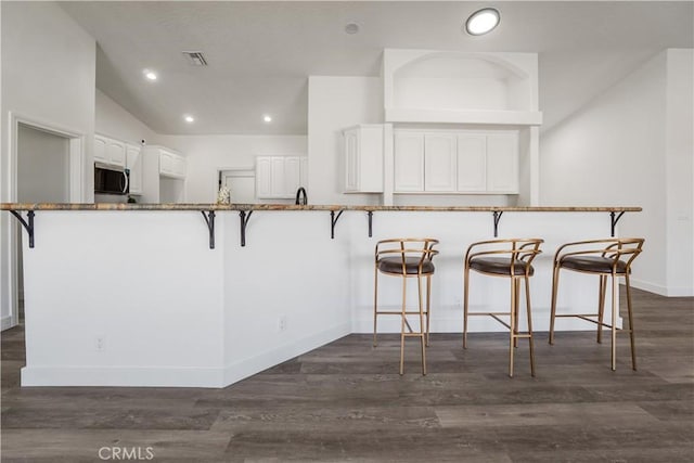 kitchen with dark hardwood / wood-style flooring, kitchen peninsula, white cabinets, and a kitchen bar