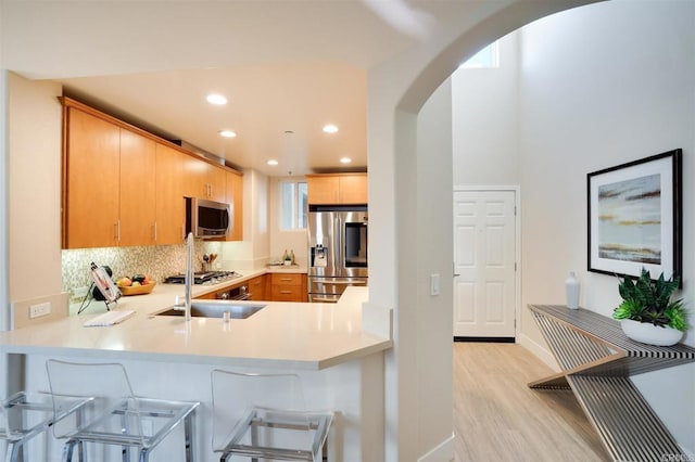 kitchen featuring a kitchen bar, light brown cabinetry, light wood-type flooring, kitchen peninsula, and stainless steel appliances