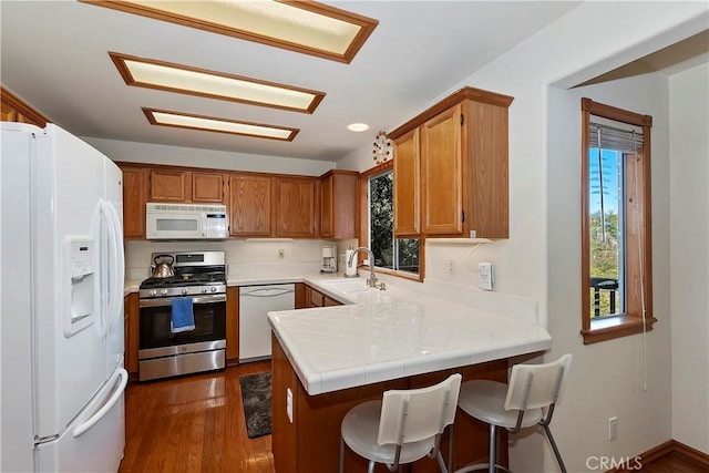 kitchen featuring sink, tile countertops, dark hardwood / wood-style floors, kitchen peninsula, and white appliances