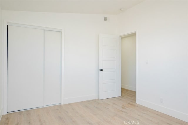 unfurnished bedroom with a closet, lofted ceiling, and light hardwood / wood-style flooring