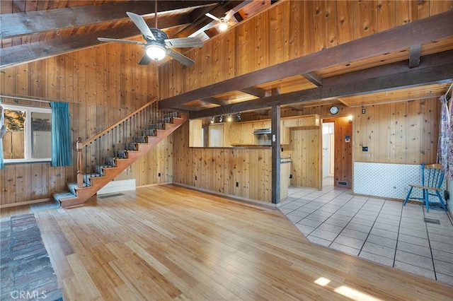 unfurnished living room featuring ceiling fan, wood walls, light hardwood / wood-style floors, and vaulted ceiling with beams