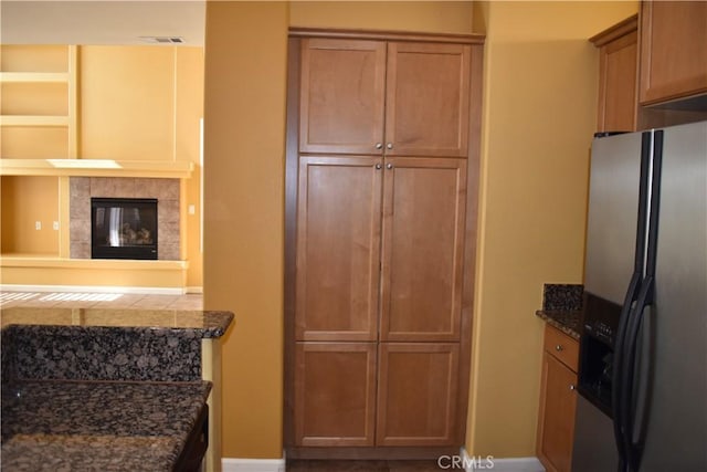 kitchen featuring a tiled fireplace, stainless steel fridge with ice dispenser, and dark stone counters