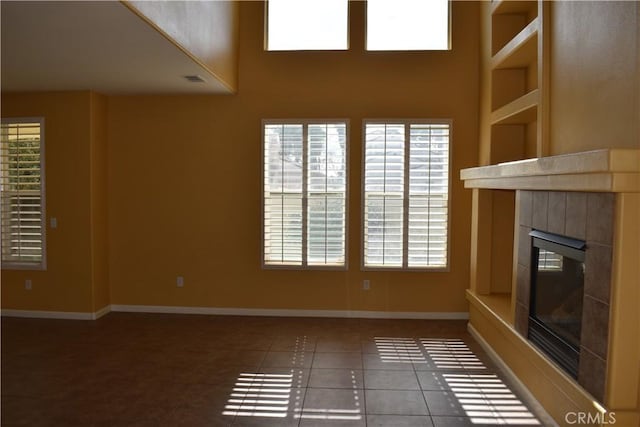 unfurnished living room with a tile fireplace, a wealth of natural light, and dark tile patterned flooring