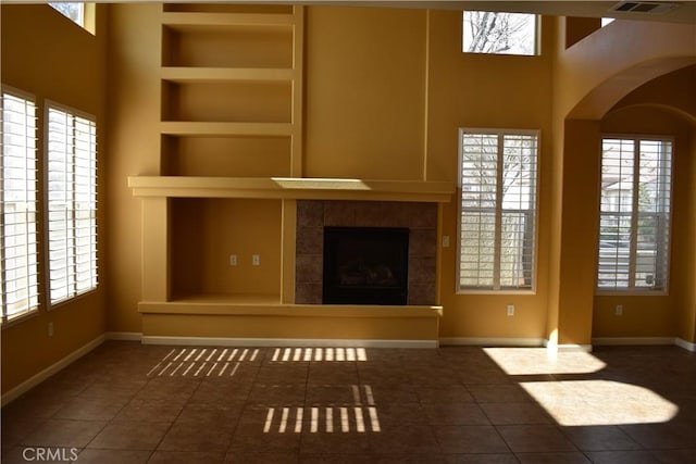 unfurnished living room with dark tile patterned floors, a towering ceiling, a fireplace, and built in shelves