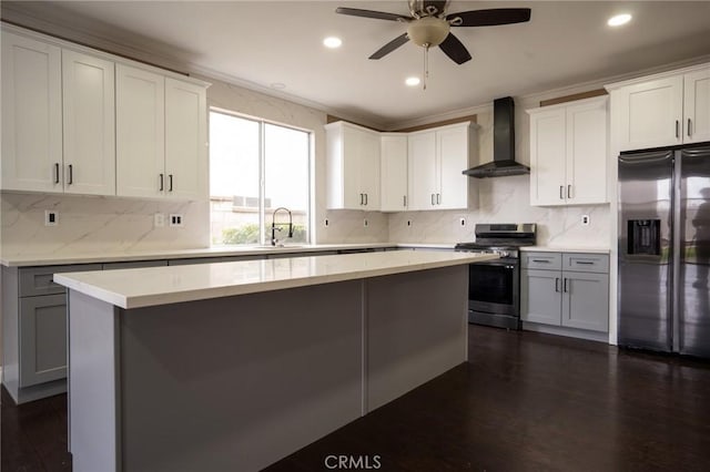 kitchen featuring wall chimney exhaust hood, sink, appliances with stainless steel finishes, a kitchen island, and white cabinets