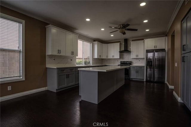 kitchen with a kitchen island, appliances with stainless steel finishes, white cabinetry, ornamental molding, and wall chimney range hood
