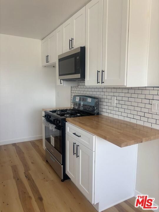 kitchen with appliances with stainless steel finishes, white cabinets, butcher block countertops, and light hardwood / wood-style flooring