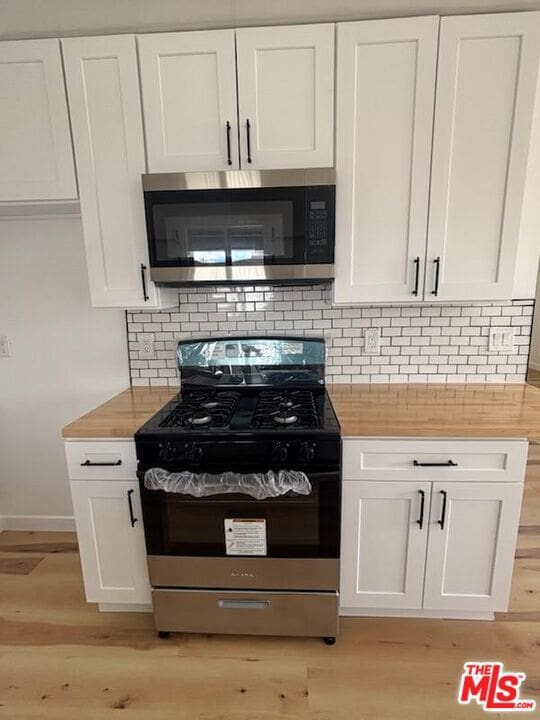 kitchen featuring range with gas cooktop, wooden counters, light hardwood / wood-style floors, decorative backsplash, and white cabinets