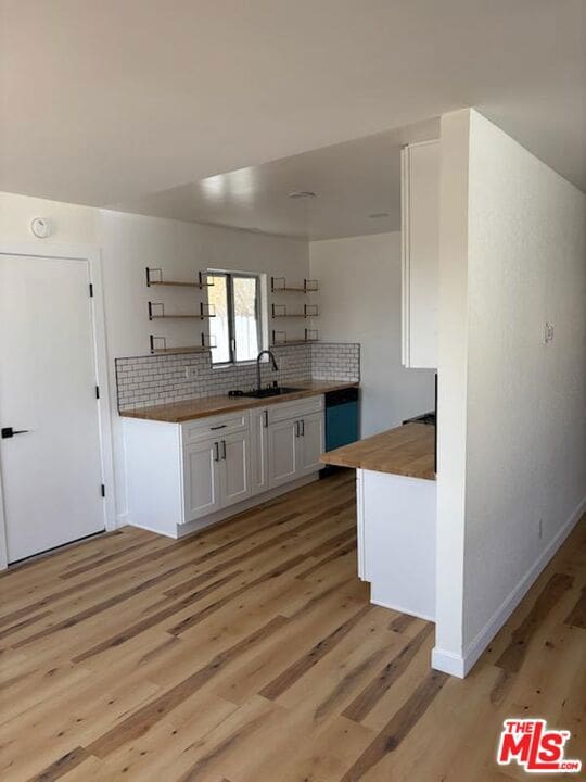 kitchen featuring white cabinetry, wooden counters, sink, and light wood-type flooring