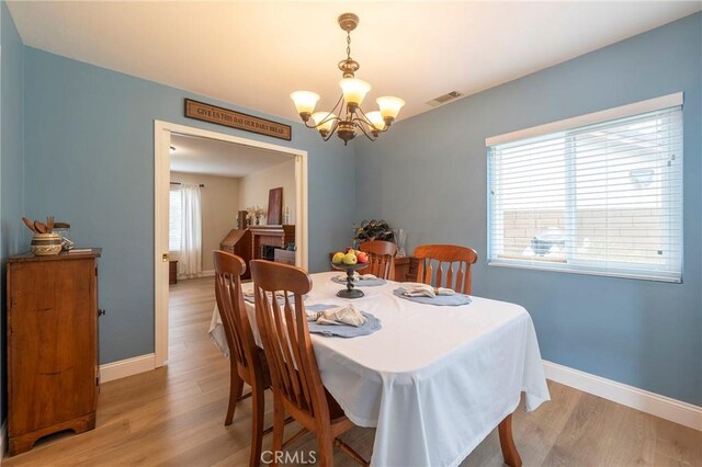 dining area featuring visible vents, a notable chandelier, baseboards, and light wood-type flooring