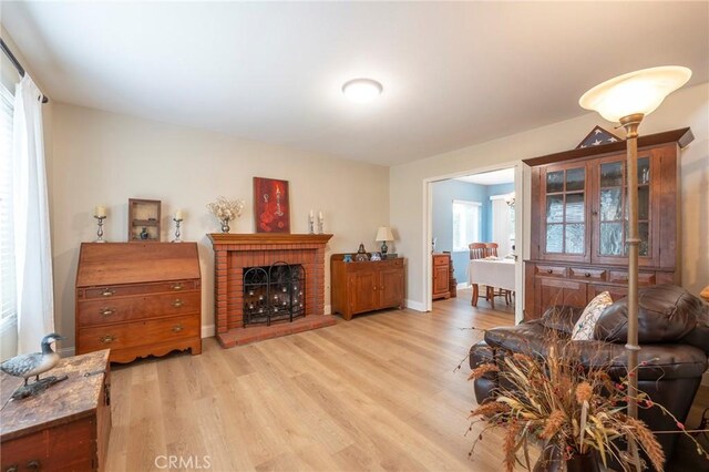 living area with baseboards, a brick fireplace, and light wood-style flooring