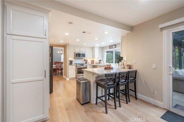 kitchen with backsplash, light countertops, a peninsula, a kitchen breakfast bar, and stainless steel appliances