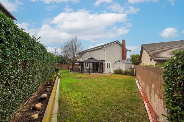 back of house featuring a gazebo, stucco siding, a lawn, and a fenced backyard