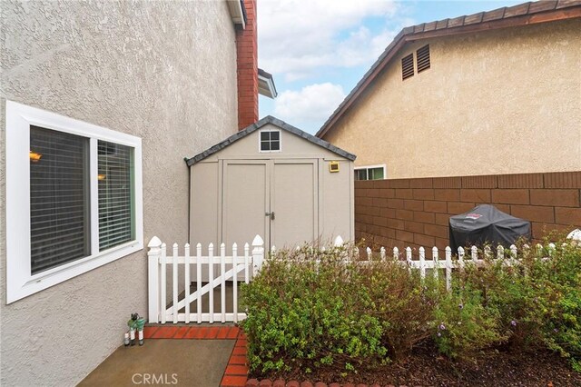 view of side of property with a shed, stucco siding, an outdoor structure, and fence