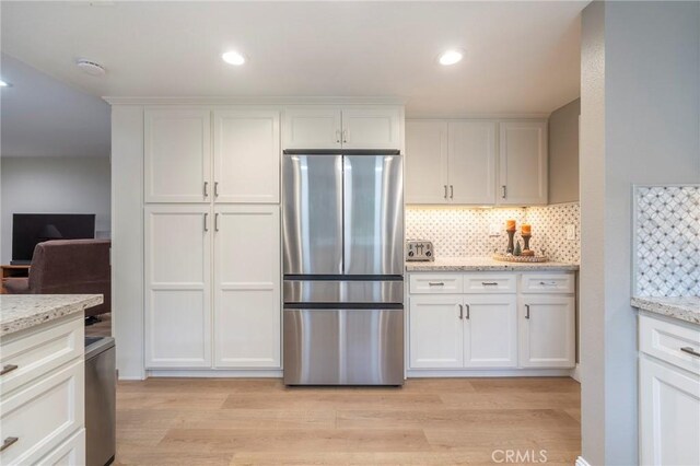 kitchen featuring light wood-style flooring, light stone counters, backsplash, white cabinetry, and freestanding refrigerator