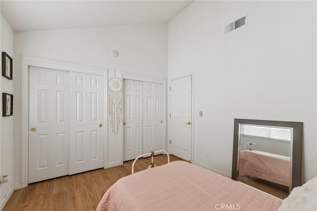 bedroom featuring multiple closets, high vaulted ceiling, and light hardwood / wood-style floors