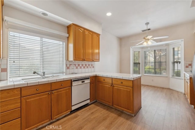 kitchen featuring tile counters, light hardwood / wood-style floors, kitchen peninsula, and dishwasher