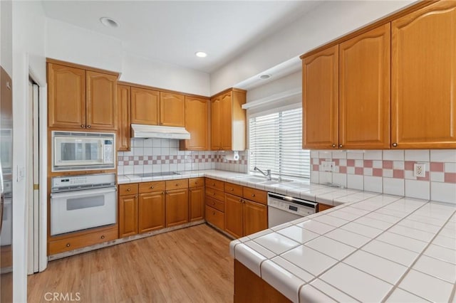 kitchen featuring tile countertops, tasteful backsplash, sink, white appliances, and light hardwood / wood-style flooring