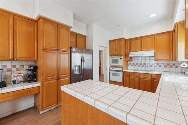 kitchen featuring white appliances, tile countertops, light hardwood / wood-style floors, and decorative backsplash