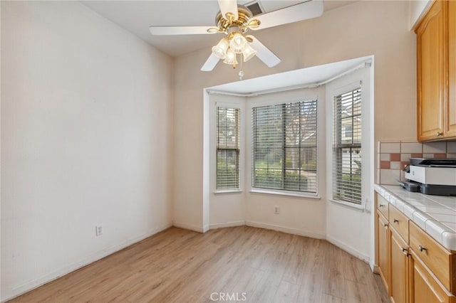 unfurnished dining area with ceiling fan and light wood-type flooring