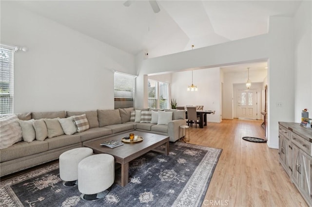 living room featuring ceiling fan with notable chandelier, light hardwood / wood-style flooring, and high vaulted ceiling