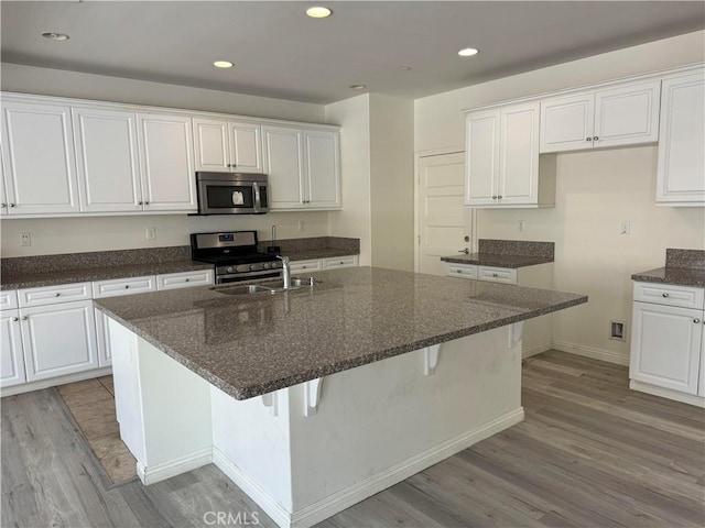 kitchen featuring an island with sink, appliances with stainless steel finishes, white cabinets, and dark stone counters