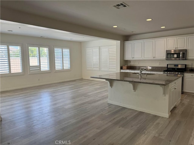 kitchen with sink, a breakfast bar area, white cabinetry, stainless steel appliances, and a kitchen island with sink