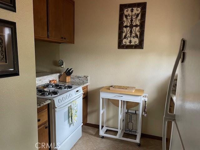 kitchen with light stone counters, white range with gas cooktop, and light tile patterned floors