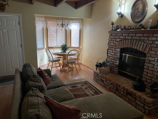 living room featuring hardwood / wood-style floors, a notable chandelier, a fireplace, and beamed ceiling