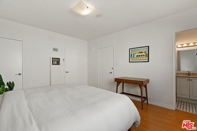 bedroom with sink, connected bathroom, and light wood-type flooring