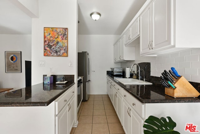 kitchen with dark stone countertops, sink, stainless steel refrigerator, and white cabinets