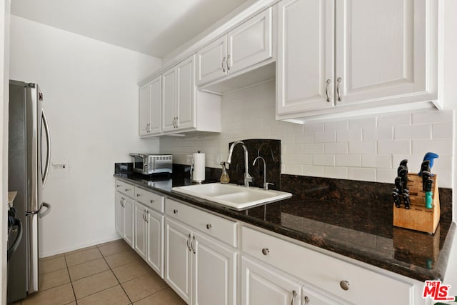 kitchen with sink, stainless steel refrigerator, white cabinetry, backsplash, and dark stone countertops