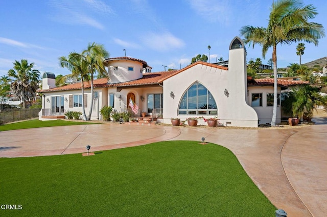 rear view of property featuring driveway, a lawn, a tile roof, and stucco siding