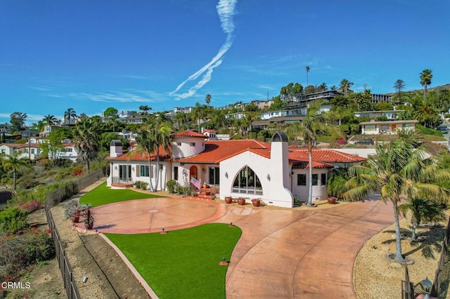 mediterranean / spanish house featuring stucco siding, concrete driveway, fence, a tiled roof, and a front lawn