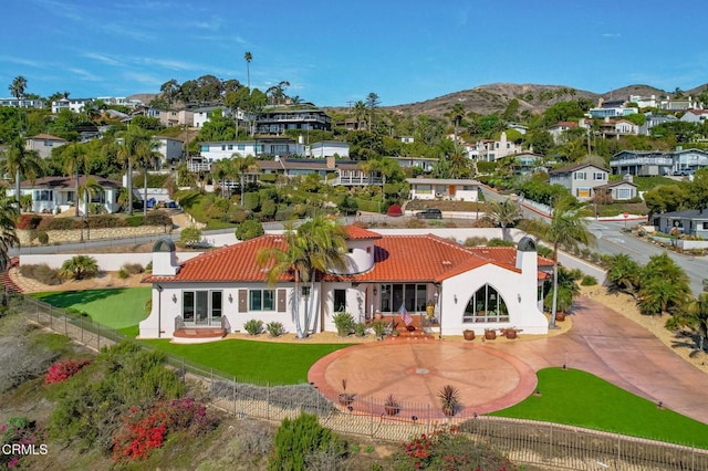 rear view of property with a tile roof, a chimney, a fenced backyard, a mountain view, and stucco siding