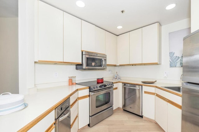 kitchen with white cabinetry, stainless steel appliances, sink, and light hardwood / wood-style flooring