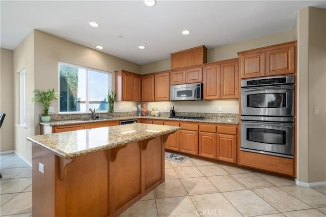 kitchen with a breakfast bar, light tile patterned floors, appliances with stainless steel finishes, a kitchen island, and light stone countertops