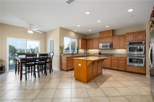 kitchen with a breakfast bar area, light stone counters, light tile patterned floors, a kitchen island, and stainless steel appliances